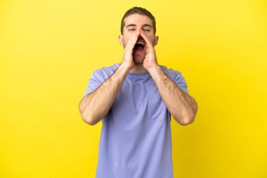 Sarışın yakışıklı adam sarı arka planda bağırıyor ve bir şeyler söylüyor.