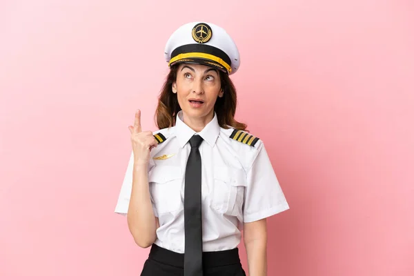 Airplane middle aged pilot woman isolated on pink background pointing up and surprised