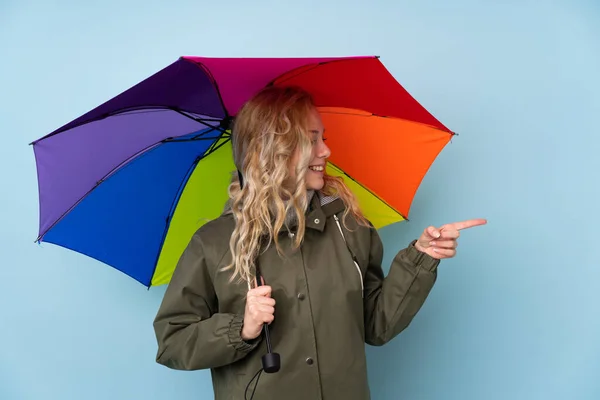 Young Blonde Woman Holding Umbrella Isolated Blue Background Pointing Side — Stock Photo, Image