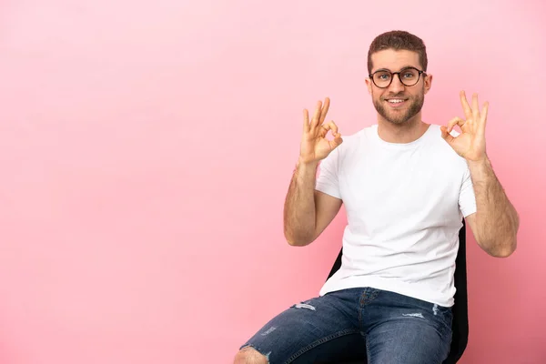 Mladý Muž Sedí Židli Nad Izolované Růžové Pozadí Ukazující Znamení — Stock fotografie