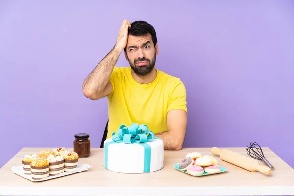 Man in a table with a big cake with an expression of frustration and not understanding