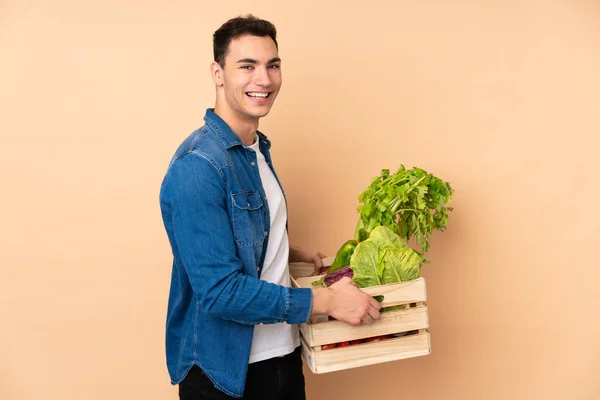 Rolnik Świeżo Zebranymi Warzywami Pudełku Izolowanym Beżowym Tle — Zdjęcie stockowe