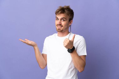 Mor arka planda izole edilmiş genç sarışın bir adam. Avucunun içinde hayali bir şey tutuyor. Bir ilan vermek için.