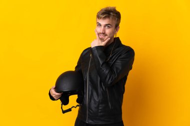 Sarı arka planda izole edilmiş motosiklet kasklı adam mutlu ve gülümsüyor.