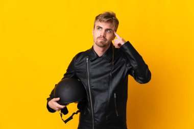 Motosiklet kasklı bir adam sarı arka planda izole edilmiş. Şüpheleri ve düşünceleri var.