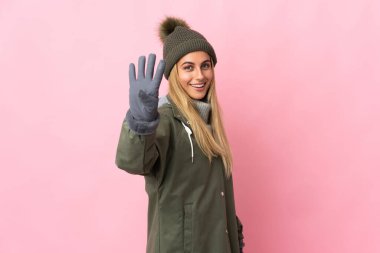 Kış şapkalı genç kadın pembe arka planda izole edilmiş mutlu ve parmakları olan dört kişi sayıyor.