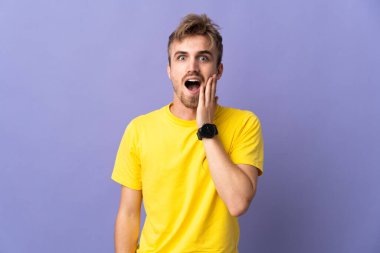 Genç yakışıklı sarışın adam, mor arka planda izole edilmiş, şaşırmış ve şok olmuş bir yüz ifadesi var.