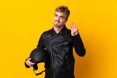Motosiklet kasklı bir adam sarı arka planda izole edilmiş mutlu ve parmaklarıyla üçe kadar sayıyor