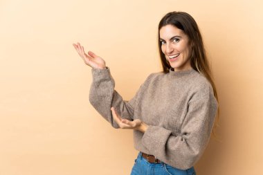 İzole edilmiş arka planda genç beyaz kadın, davet edilmek için ellerini yana uzatıyor.