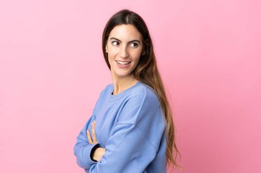 Pembe arka planda soyutlanmış genç beyaz kadın yana bakıyor ve gülümsüyor.