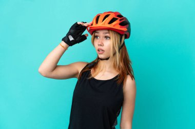 İzole edilmiş mavi arka planda, sürpriz bir ifadeyle genç bisikletçi kız.