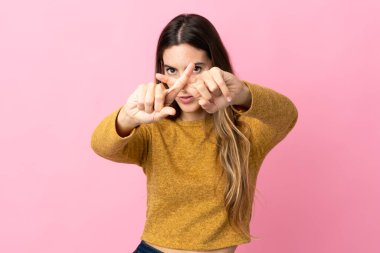 Pembe arka planda izole edilmiş genç beyaz kadın bir hareketi durdurmak için eliyle jest yapıyor.