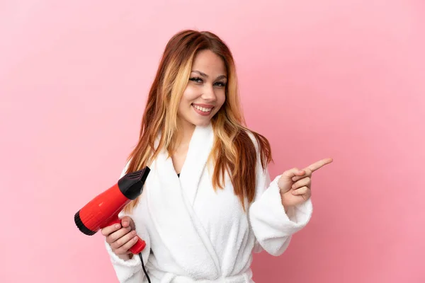 Adolescente Loira Segurando Secador Cabelo Sobre Fundo Rosa Isolado Apontando — Fotografia de Stock