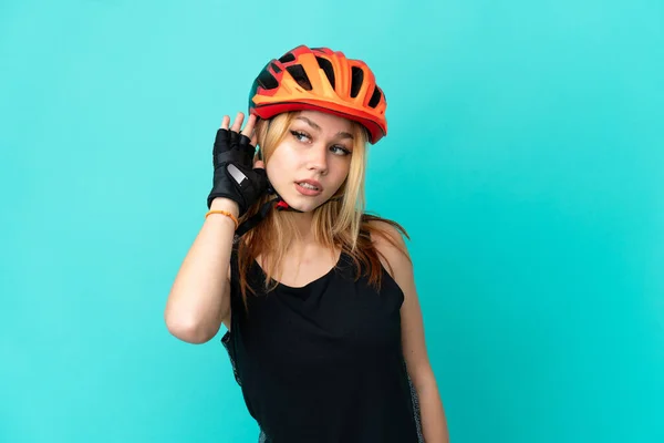Młoda Rowerzystka Nad Odizolowanym Niebieskim Tle Słuchając Czegoś Kładąc Rękę — Zdjęcie stockowe