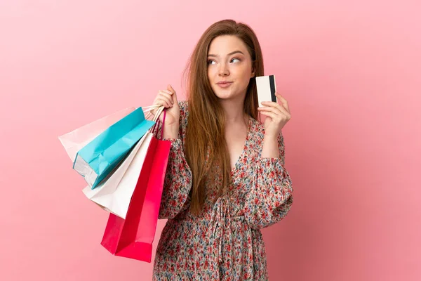 一个年轻女孩 背负着购物袋和信用卡 独自面对粉色背景 她在想 — 图库照片