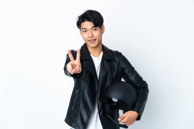 Beyaz arka planda izole edilmiş motosiklet kasklı Çinli adam gülümsüyor ve zafer işareti gösteriyor.