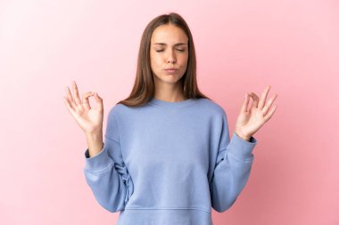 Zen pozisyonunda soyutlanmış pembe arka planı olan genç bir kadın.