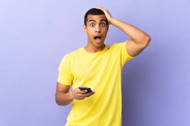 Yüzünde sürpriz ifade olan cep telefonu kullanan, izole edilmiş mor arka planda yaşayan Afrikalı Amerikalı bir adam.
