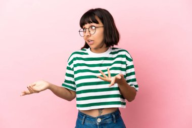 Pembe arka planda soyutlanmış genç melez bir kadın sürpriz bir ifadeyle yan tarafa bakıyor.