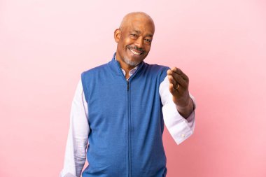 Kübalı son sınıf öğrencisi pembe arka planda izole edilmiş, iyi bir anlaşma için el sıkışıyor.