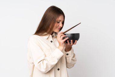 Beyaz arka planda izole edilmiş beyaz tenli genç bir kız elinde çubuklarla bir kase erişte tutuyor ve onu yiyor.