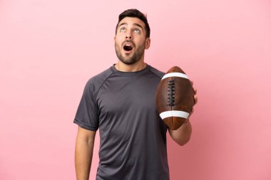 Pembe arka planda ragbi oynayan beyaz bir genç yukarı bakıyor ve şaşırmış bir ifadeyle