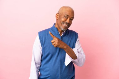 Kübalı son sınıf öğrencisi pembe arka planda izole edilmiş bir ürün sunmak için yan tarafı işaret ediyor