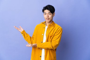 Mor arka planda izole edilmiş genç bir Çinli davet etmek için ellerini yana uzatıyor.