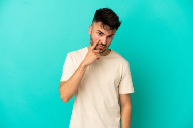 Mavi arka planda izole edilmiş genç beyaz bir adam bir şey gösteriyor.