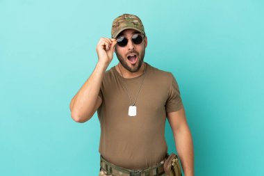 Mavi arka planda izole edilmiş, gözlüklü ve şaşırmış asker.