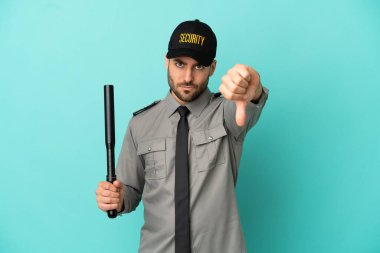 Mavi arka planda izole edilmiş genç bir güvenlik görevlisi, olumsuz ifadeyle baş parmağını gösteriyor.