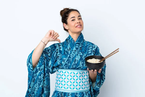 Woman wearing kimono over isolated white background proud and self-satisfied while holding a bowl of noodles with chopsticks