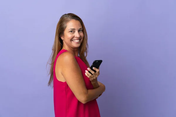 携帯電話を持っている紫色の背景に隔離された中世のブラジル人女性と腕を組んで交差 — ストック写真