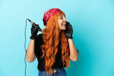 Dövme sanatçısı melez kadın mavi arka planda izole edilmiş ağzı sonuna kadar açık bağırıyor.