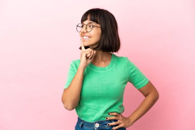 Genç melez kadın pembe arka planda izole edilmiş bir şekilde bakarken bir fikir düşünüyor.