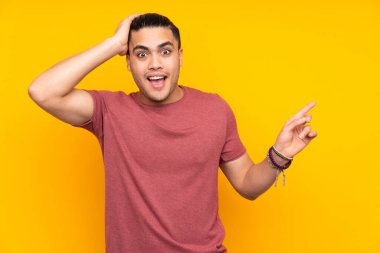 Sarı arka planda izole edilmiş Asyalı yakışıklı bir adam bir ürün sunmak için kenarı işaret ediyor.