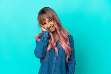 Mavi arka planda pembe saçlı melez bir kadın gülüyor.