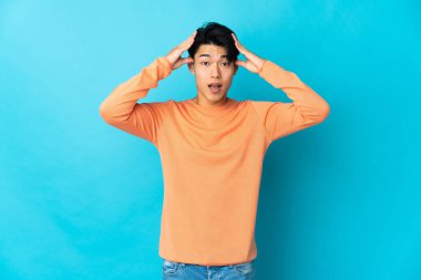 Mavi arka planda, sürpriz bir ifadeyle izole edilmiş genç bir Çinli.