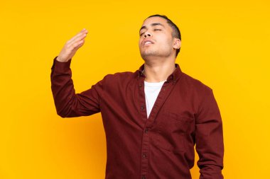 Asyalı yakışıklı adam sarı arka planda izole edilmiş. Davet etmek için ellerini yana uzatıyor.