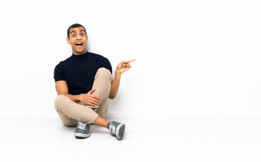 Afro-Amerikan adam yerde oturuyor, şaşırmış ve işaret ediyor.