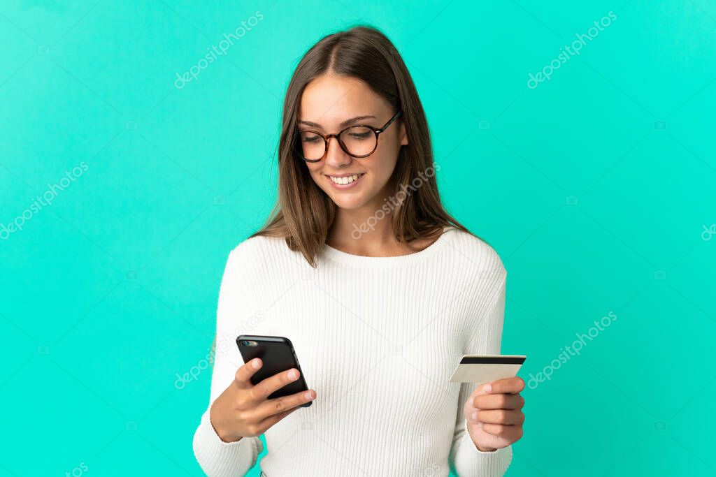 Young woman over isolated blue background buying with the mobile with a credit card