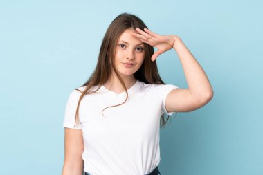 Genç beyaz kız mavi arka planda izole edilmiş mutlu bir ifadeyle selamlıyor.