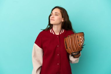 Beyzbol oynayan beyaz bir kadın. Mavi arka planda izole edilmiş. Yan tarafa bakıyor.