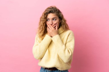 Genç sarışın kadın pembe arka planda izole edilmiş ağzını kapatıyor ve yan tarafa bakıyor.