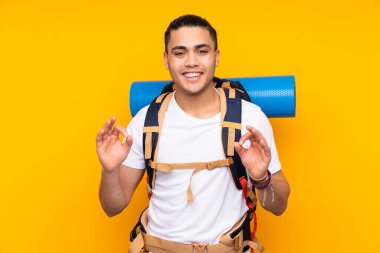 Sarı arka planda izole edilmiş büyük sırt çantalı Asyalı genç adam parmaklarıyla 