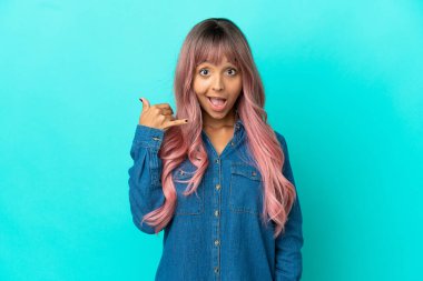 Mavi arka planda izole edilmiş pembe saçlı melez bir kadın telefon jesti yapıyor. Bana geri dönüş işareti ver.