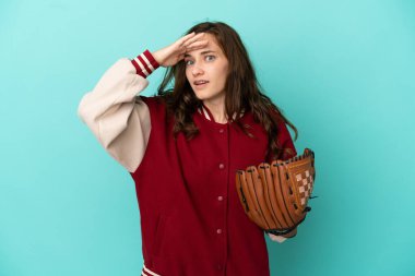 Beyzbol oynayan beyaz bir kadın. Mavi arka planda izole edilmiş. Yan tarafa bakarken sürpriz jest yapıyor.