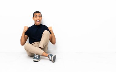 Afro-Amerikalı adam yerde oturmuş galibiyeti kutluyor.