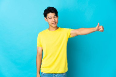 Mavi arka planda izole edilmiş genç bir Çinli baş parmak işareti yapıyor.