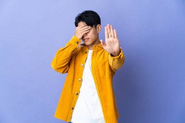 Mor arka planda izole edilmiş genç Çinli adam dur hareketi yapıyor ve yüzünü kapatıyor.